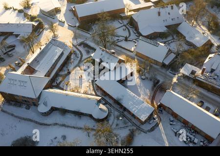 Drohnenblick auf einen verschneiten Bauernhof in Deutschland mit Scheunen und Häusern unter frischem Winterschnee, langen Schatten und gewundenen Wegen im Krieg Stockfoto
