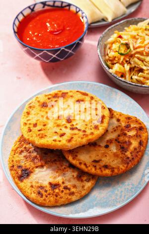 Tischdecke mit Blick auf die lateinamerikanische Küche mit Pupusas, Arepas, Curtido, Humitas, Yuca und Salsa auf einem farbenfrohen rosafarbenen Tisch für ein Familienessen. Stockfoto