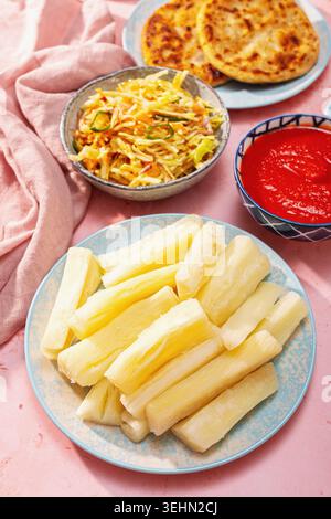 Gekochter Yuca in der Mitte eines farbenfrohen lateinamerikanischen Tisches, serviert mit Pupusas, Humitas, Curtido Slaw und roter Salsa, perfekt für einen festlichen Urlaub Stockfoto