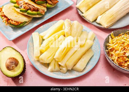 Gekochter Yuca in der Mitte eines farbenfrohen lateinamerikanischen Esstisch mit Pupusas, Humitas, Curtido und Avocado, gestylt für ein festliches Weihnachtsessen. Stockfoto
