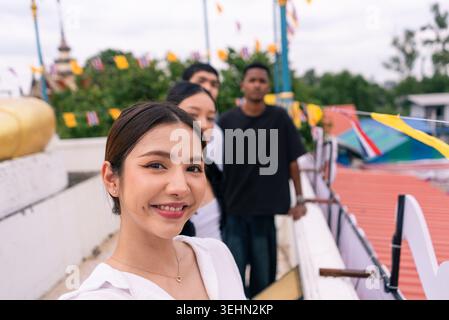 Junge asiatische Frau lächelt und nimmt Selfie mit verschiedenen Freunden auf dem Dach des Tempels Stockfoto