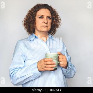 Frau mittleren Alters hält eine Kaffeetasse und sieht nachdenklich in einem lässigen Innenporträt aus Stockfoto
