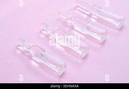 Transparente Glasampullen mit klarer Flüssigkeit auf weichem rosa Hintergrund, Draufsicht, minimale Zusammensetzung, glatte Textur, Kopierraum Stockfoto
