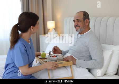 Die Pflegekraft frühstückt einem älteren Mann zu Hause im Bett Stockfoto