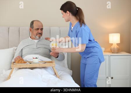 Die Pflegekraft frühstückt einem älteren Mann zu Hause im Bett Stockfoto