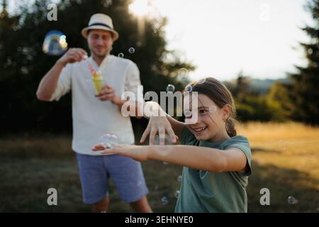 Vater und Tochter spielen bei Sonnenuntergang draußen mit Seifenblasen. Stockfoto
