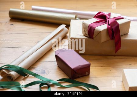 Nahaufnahme mit gestapelten Geschenkkartons aus Kraftpapier mit tiefroter Satinschleife auf der Tischplatte Stockfoto