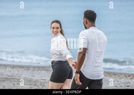 Ein paar Spaziergänge Hand in Hand entlang Playa del Zapillo, lächelnd und genießen den wunderschönen Strand in Almeria, Spanien. Das ruhige Wasser und der sonnige Himmel schaffen das Stockfoto