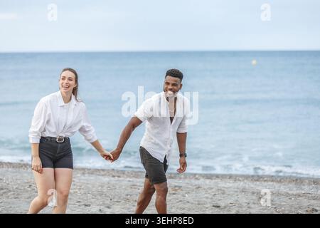 Ein fröhliches Paar spaziert Hand in Hand entlang der Sandküste von Playa del Zapillo in Almeria, Spanien, lächelt und genießt die Gesellschaft des anderen. Die Kalibration Stockfoto