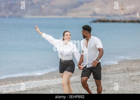 Ein paar Spaziergänge Hand in Hand entlang der Küste von Playa del Zapillo, Almeria, Spanien, mit der Sonne darüber. Sie lachen und engagieren sich eindeutig Stockfoto