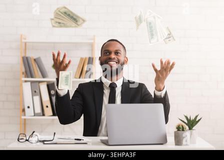 Emotionaler junger Geschäftsmann im Anzug, der am Arbeitsplatz Geld vergießt Stockfoto
