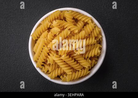 Essen, rohe Fusilli-Pasta aus Vollkornweizensorten auf dunklem texturiertem Hintergrund Stockfoto