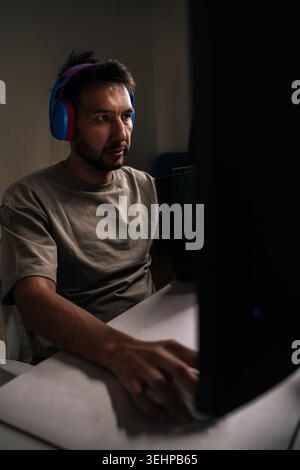 Porträt eines bärtigen männlichen Spielers in Kopfhörern, der Videospiele auf dem Desktop-Computer spielt, sich auf den Bildschirm konzentriert, Inhalte erstellt, streamt, mitspielt Stockfoto