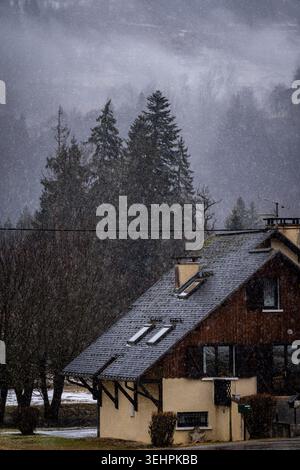 Schnee über einem gemütlichen Almchalet umgeben von Bäumen in den französischen Alpen im Winter. Stockfoto