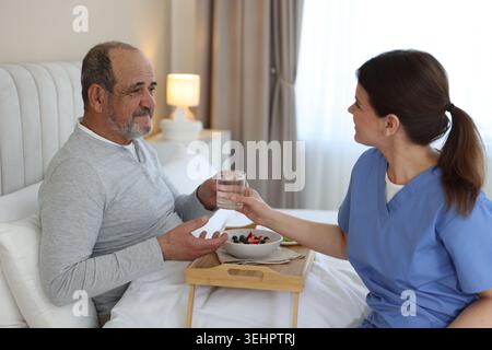 Die Pflegekraft frühstückt einem älteren Mann zu Hause im Bett Stockfoto