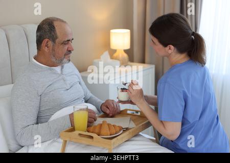Die Pflegekraft frühstückt einem älteren Mann zu Hause im Bett Stockfoto