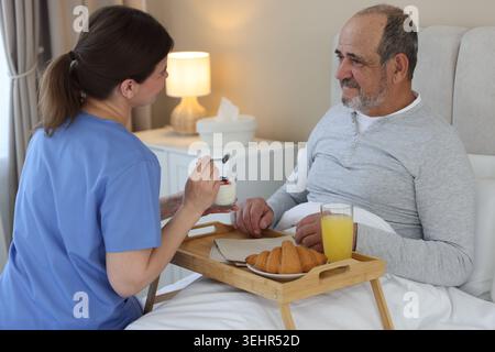 Die Pflegekraft frühstückt einem älteren Mann zu Hause im Bett Stockfoto
