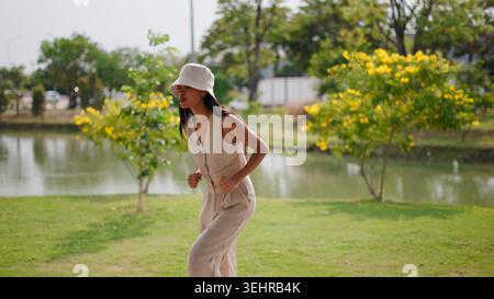 Frau tanzt draußen in einem Park neben einem Teich mit gelb blühenden Bäumen Stockfoto