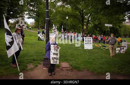 Boston, Massachusetts, USA. 25. Mai 2026. Mehr als 50 Soldaten, die gegen den Krieg protestierten, versammelten sich am Memorial Day an der Metro Station am Boston Common und marschierten dann durch den Park zum Soldiers and Sailors Monument auf dem Flag Staff Hill im Zentrum des Parks. Am Fuße des Hügels legten die Veteranen hauptsächlich Kinderschuhe, Spielzeug und Blumen an. Die Demonstranten haben abwechselnd die Namen der Kinder gelesen, die infolge der Bombardierung des Iran gestorben sind. Foto: Mary, 68, steht mit einem selbstgemachten Schild mit der Aufschrift „Stop the war“, während die Namen gelesen werden. Quelle: Chuck Nacke / Alamy Live News Stockfoto