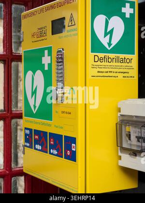 Eine Hand gibt den Code auf einem hellgelben Community Heartbeat-AED-Defibrillator in einer umfunktionierten roten britischen Telefonbox in England ein. Stockfoto
