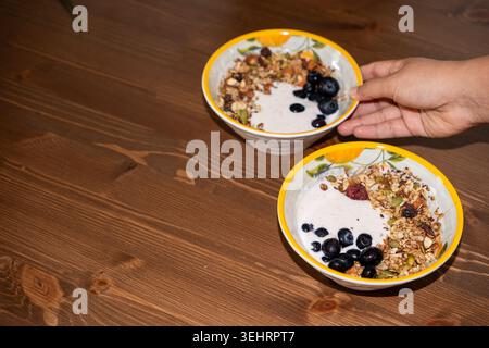 Handservieren Sie gesunde Smoothie-Schüsseln mit Müsli und Heidelbeeren auf Holztisch Stockfoto