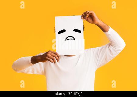 Schwarzer Mann, Papier mit traurigen Emoji über sein Gesicht Stockfoto