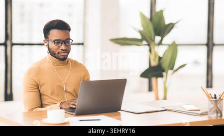 Konzentrierter Afro-Typ in Brillen, der auf der Tastatur schreibt Stockfoto