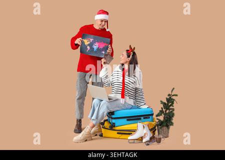 Nettes junges Paar mit Weltkarte, Laptop, Pässen und Koffern auf beigefarbenem Hintergrund. Winterurlaubskonzept Stockfoto