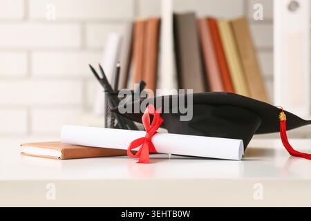 Diplom mit Buch und Mörtelplatte auf weißem Tisch Stockfoto