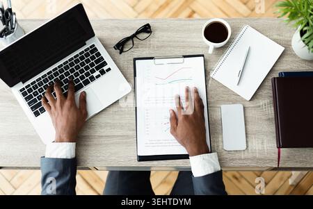 Business Professional analysiert Daten auf einem Laptop an einem Holzschreibtisch in einem modernen Büro Stockfoto