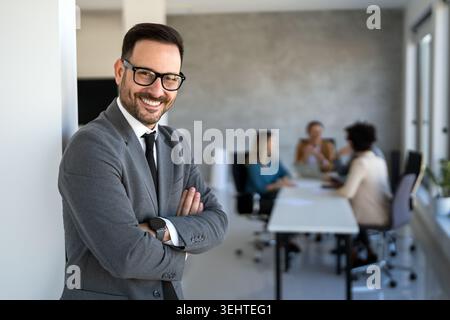 Gutaussehender junger Geschäftsmann, der vor seinem Team selbstbewusst im Firmenbüro steht Stockfoto