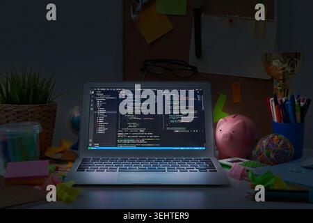 Arbeiten Sie spät an Programmieraufgaben an einem Schreibtisch mit farbenfrohen Verbrauchsmaterialien und einem Laptop Stockfoto