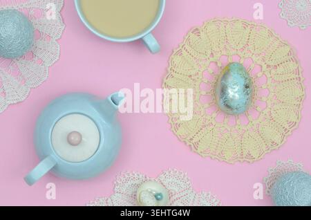 Pastellfarben auf dem Tisch: Osterdekoration mit blauen Ostereiern, Spitze, gelb, Vintage Serviette, Tasse Kaffee und blaue Teekanne auf rosa Tisch. Stockfoto