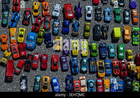 POLOP, Spanien - 10. Mai 2026. Verschiedene Spielzeugautos sind auf grauem Asphalt verteilt. Die Autos sind in vielen Farben und Formen gehalten und zeigen ein geschäftiges Arrangement Stockfoto