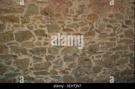 Eine alte rustikale Steinmauer aus unregelmäßigen braunen Tonziegeln und Mörtel, typisch für mediterrane Architektur. Die Wand hat einen verwitterten Look. Stockfoto
