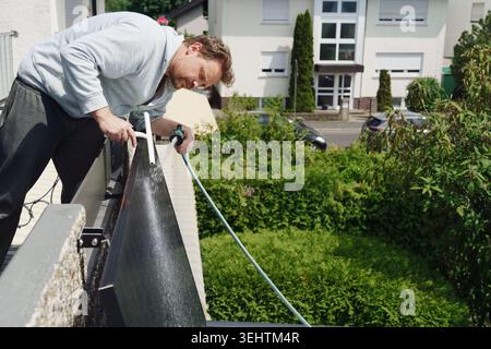 Ein Mann, der an einem sonnigen Tag Sonnenkollektoren auf einem Balkon-Kraftwerk reinigt. Stockfoto