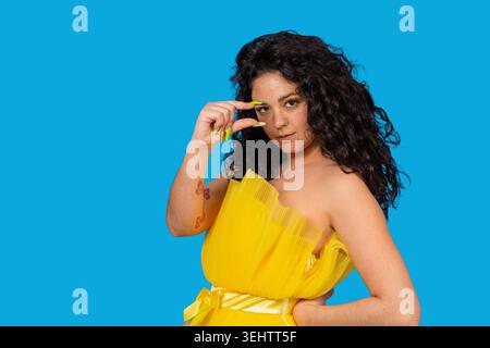 Junge Frau in gelbem Kleid mit lockigem Haar, die eine Messgeste mit Fingern macht Stockfoto