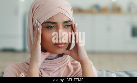 Traurige frustrierte indische arabische muslimische Frau im Hijab denkt Kopf in Innenräumen halten weibliche islamische Mädchen, die krank ist, gestresste Migräne Kopfschmerzen Stockfoto