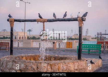 Traditioneller Steinbrunnen mit Tauben in Doha, Katar, mit alter Holzkonstruktion und Eimer auf dem historischen Platz am frühen Morgen. Stockfoto