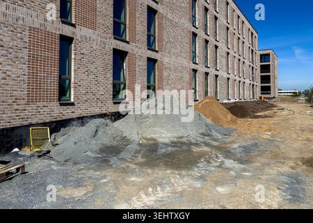 Die Arbeiter bereiten den Standort für ein neues Gebäude vor. Auf dem Boden befinden sich Sand-, Kies- und Schmutzhaufen. Der Himmel ist klar und blau. Die Baustelle ist in Betrieb Stockfoto