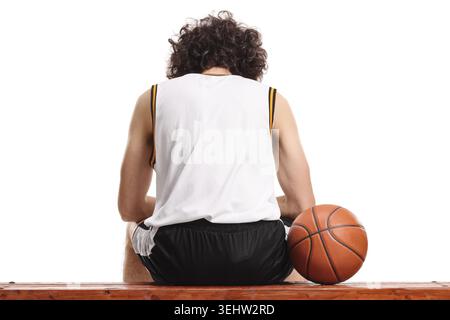 Rückansicht eines Basketballspielers, der auf einer Bank sitzt und einen Ball auf weißem Hintergrund isoliert hat Stockfoto
