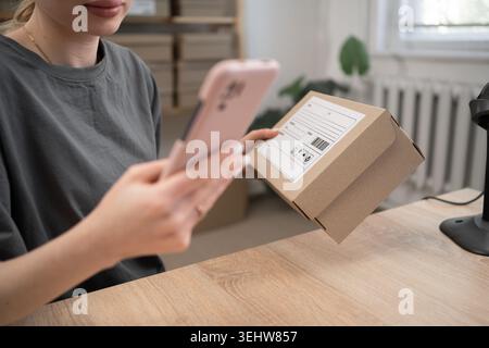 Lagerarbeiterin, die Box und Telefon hält und die Lieferkette im Vertriebsbüro für das Scannen von Barcodes vorbereitet. Logistik für die Lieferung. Nahaufnahme Stockfoto