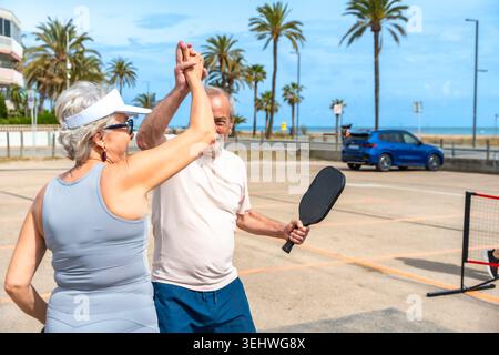 Seniorenpaar High Fiving beim Pickleball am Strand Stockfoto