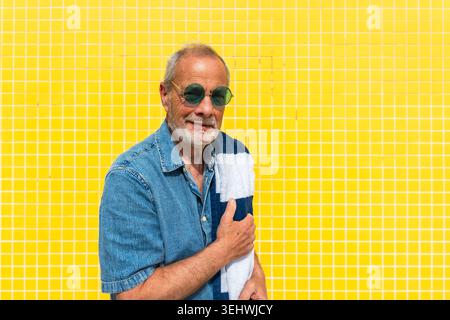 Senior Mann lächelte mit Sonnenbrille und Strandtuch Stockfoto