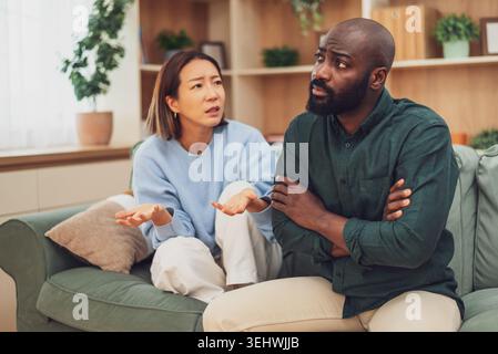Multirassisches erwachsenes Paar, das auf der Couch in ihrer Wohnung sitzt und einen Streit hat. Sie sind wütend auf einander. Stockfoto