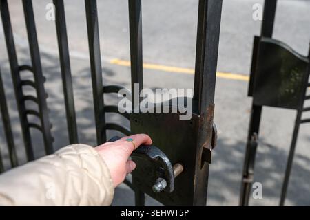 Nahaufnahme eines von Hand öffnenden schwarzen schmiedeeisernen Tors auf sonniger Stadtstraße mit selektivem Fokus und minimaler Komposition Stockfoto