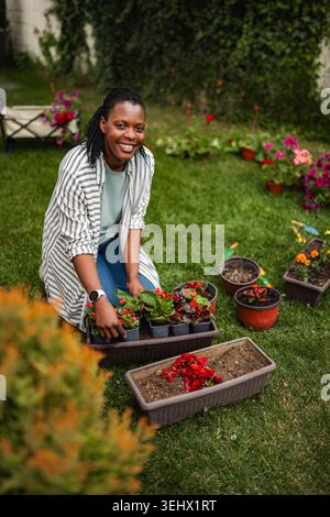 Glückliche junge Erwachsene Frau, die Blumen im Garten pflanzt Stockfoto