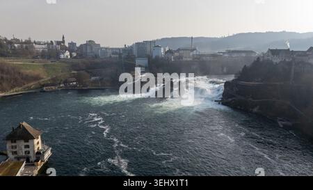 Luftaufnahme des Rheinfalls mit turbulentem Flusswasser, Nebel, Brücken und Stadtgebäuden in der Nähe von Schaffhausen, Schweiz. Stockfoto