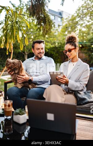 Ein Paar, das sich mit einem Hund entspannt und draußen an einem Laptop-Tablet arbeitet Stockfoto