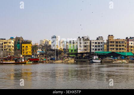 Blick aufs Wasser auf einen belebten Küstensteg mit farbenfrohen Wohngebäuden, angedockten Passagierfährschiffen und Wasserreflexionen, Mumbai, Indien Stockfoto
